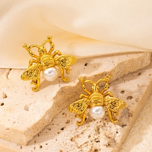 Detail of vintage gold bee earring with white pearl on textured stone and silk background