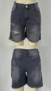 Dettaglio di pantaloncini in denim grigio slavato a vita alta con fori e orli a frange