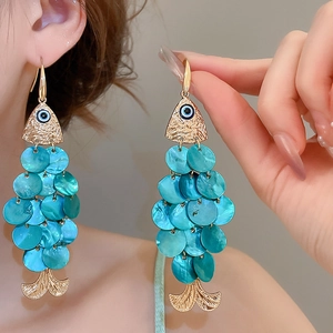 Detail of golden fish earrings with blue shell scales worn by a model in soft lighting