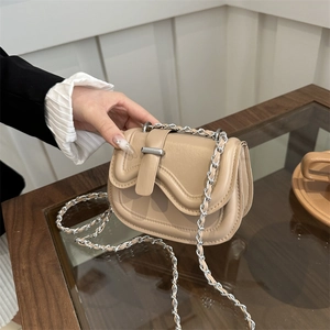 Minimalist beige faux leather saddle bag with silver chain strap shown in a modern home setting