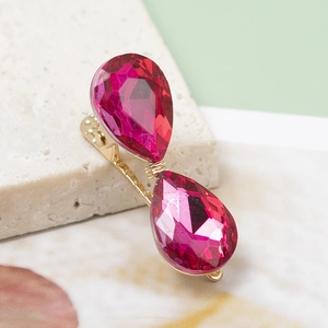 Eleganter goldener Haarclip mit zwei rosa Tropfenkristallen auf steinernem Grund