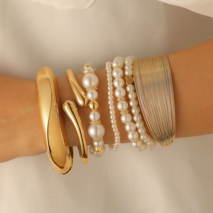 Detailed view of layered gold bangles and white pearl bracelets on a woman's wrist