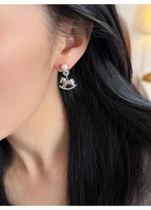 Detailed close-up of a silver horse earring with pearl and diamonds on a model's ear