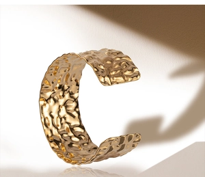 Detailed view of wide open bangle with unique hammered gold texture and shadow effects
