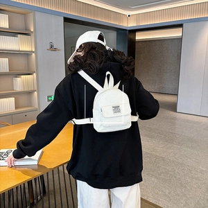 Rear view of white corduroy mini backpack worn by model in a modern indoor setting