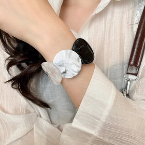 Detail of round acrylic marble and matte beads bracelet worn on wrist with beige shirt