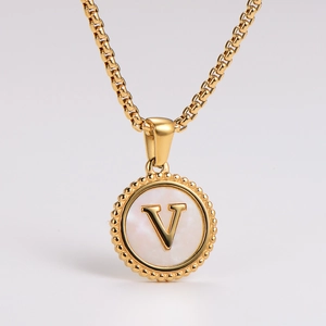 Macro shot of gold necklace featuring a round pendant with mother of pearl and V letter