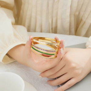 Close-up of four gold stainless steel bangles set with colorful rectangular gemstones