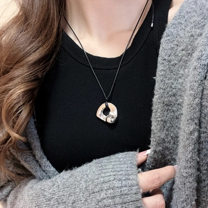 Close-up of polished silver fluid pendant on a minimalist black cord necklace