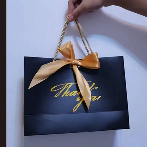 Detail of black gift bag with gold bow, woven handles, and Thank You gold lettering