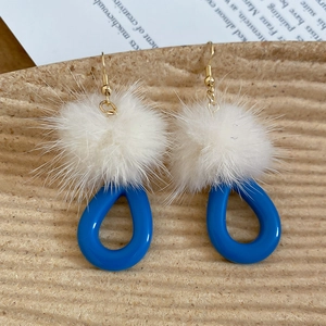Detail of winter earrings with white fur balls and royal blue resin teardrop pendants