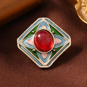 Macro detail of a vintage rhombus brooch with colorful enamel and a red center gemstone