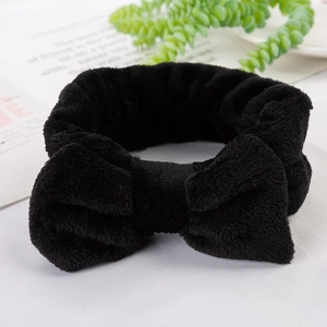 Close-up of black plush headband featuring a large bow on a minimalist white surface
