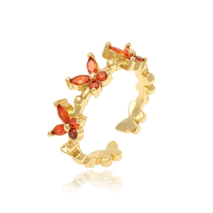 Detail shot of a gold butterfly ring with vibrant orange-red gemstones on a white base