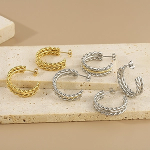 Detailed view of twisted C-shaped hoop earrings in gold and silver finish on stone