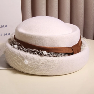 Detail of white wool beret featuring brown satin bow and elegant mesh veil with pompoms