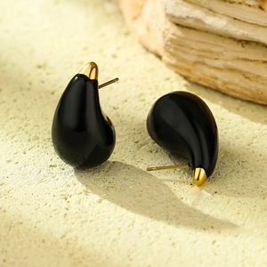 Detail showing high-polish gold and black teardrop earrings on a textured stone surface