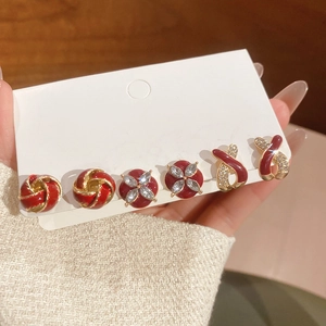 Detail of red enamel and gold stud earring set featuring floral and knot designs