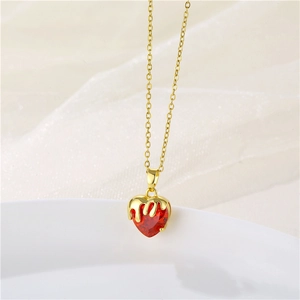 Detailed close-up of a gold necklace with a red heart crystal pendant on white fabric