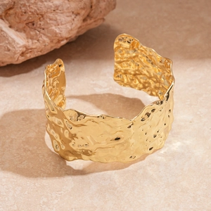 Close-up of golden cuff bracelet with irregular hammered texture on a stone surface
