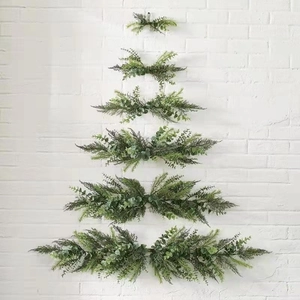 Christmas tree shaped wall hanging made of artificial pine and eucalyptus leaves on white brick