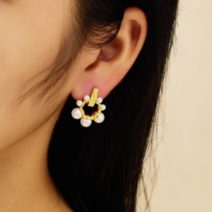 Close-up of elegant gold geometric earrings with pearls worn by a model in soft light