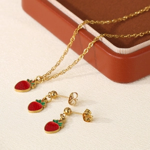 Detailed macro view of enamel strawberry pendants and earrings on beige textured fabric
