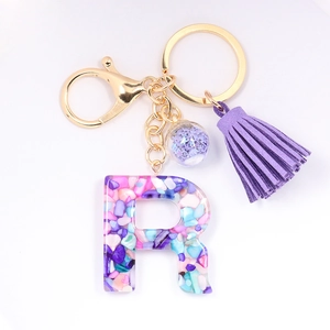 Detail of resin letter R keychain with colorful stones, purple tassel and gold clasp