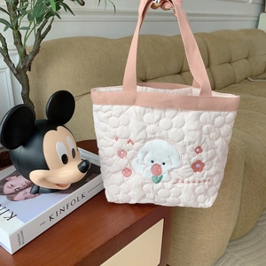 Detailed quilted texture of a pink floral tote bag with cute dog embroidery on a desk