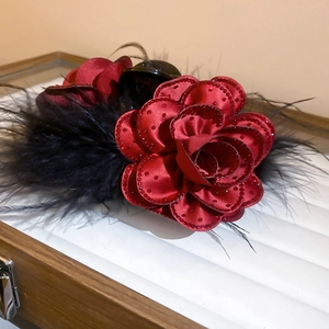 Detailed close-up of a red satin rose hair claw with black feathers and rhinestones