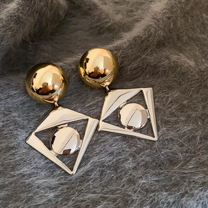 Detailed view of gold geometric drop earrings with hollow rhombus on plush background