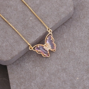 Macro shot of 18K gold butterfly necklace with purple stones on a grey stone background