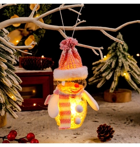 Detail of a glowing Christmas snowman ornament with pink knit hat on a snowy pine branch