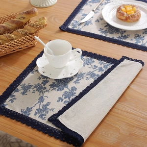 Blue rose floral linen placemat with lace edges on a rustic wooden dining table