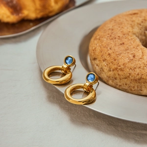 Macro detail of 18K gold stainless steel hoop earrings featuring blue zircon accents
