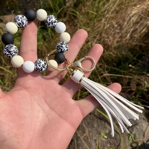Detail of beaded keychain bracelet with leopard print beads, gold ring, and white tassel