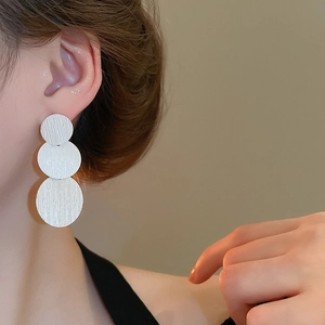 Detail of silver triple disc earrings with brushed metal texture worn by a model