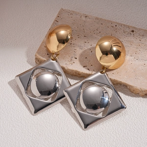 Macro shot of geometric two-tone metal earrings with gold studs and silver square pendants