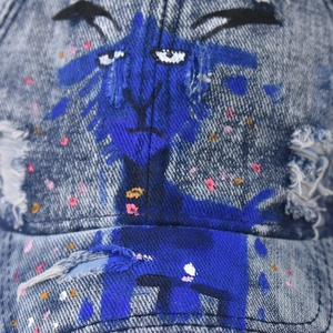 Distressed denim baseball cap with hand-painted blue sheep graffiti and ink splatter