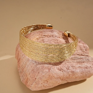 Detail of gold multi-layer woven chain open cuff bracelet on a natural stone display