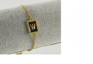 Détail d'un bracelet en acier doré avec un pendentif en émail noir arborant la lettre W