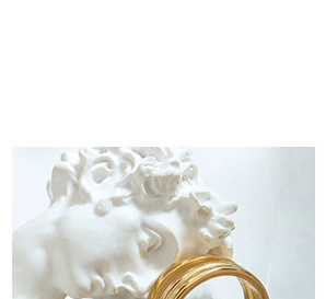 Artistic close-up of glossy gold twisted hoop earrings on white plaster statue