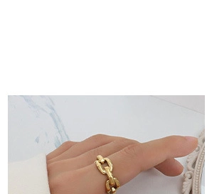 Close-up of a gold Cuban link chain ring worn on a finger over a marble background