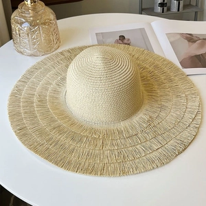 Beige wide brim straw hat with fringe edge on a white table for summer vacation