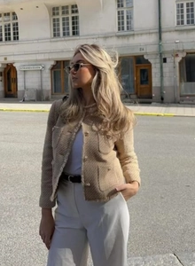 Detail of tweed short jacket in khaki showing woven texture and metal buttons on a street