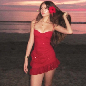 Red sequin mini dress with ruffles and slim fit design shown against a sunset beach backdrop