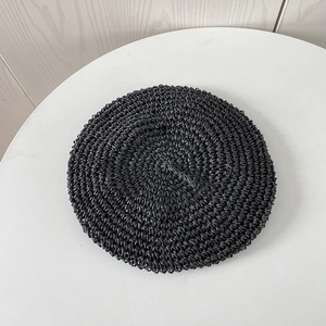 Top view of a black hand-woven straw beret hat with detailed crochet texture on white table