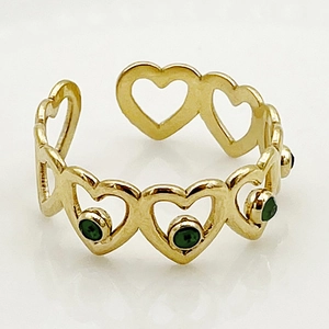 Close-up of golden stainless steel chain ring with hollow hearts and green gemstones