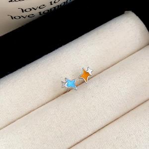 Détail macro de boucles d'oreilles étoile en émail bleu et orange sur boîte beige texturée