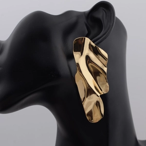 Close-up of oversized golden irregular wave earrings with a mirror-polished metallic finish